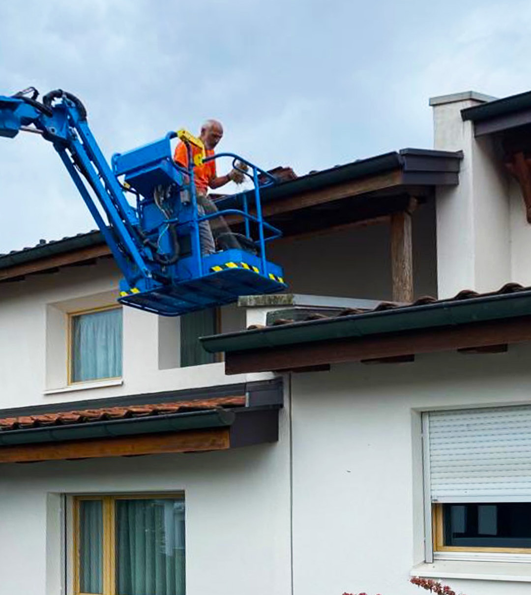Mitarbeiter auf einer Hubarbeitsbühne bei Arbeiten an der Dachkante eines Wohnhauses