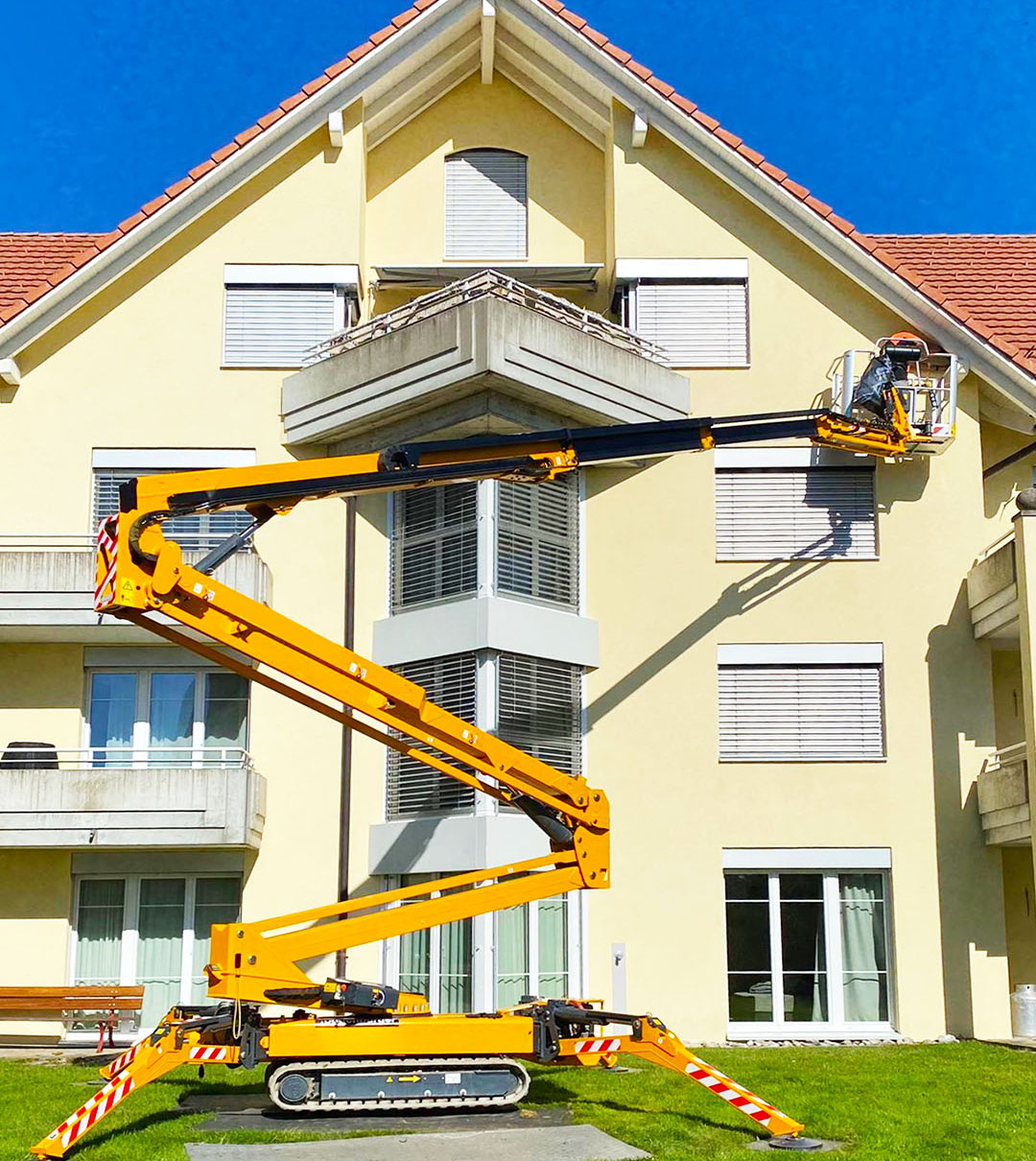 Mitarbeiter auf einer Gelenkarbeitsbühne an Fassade und Dachbereich eines Wohnhauses