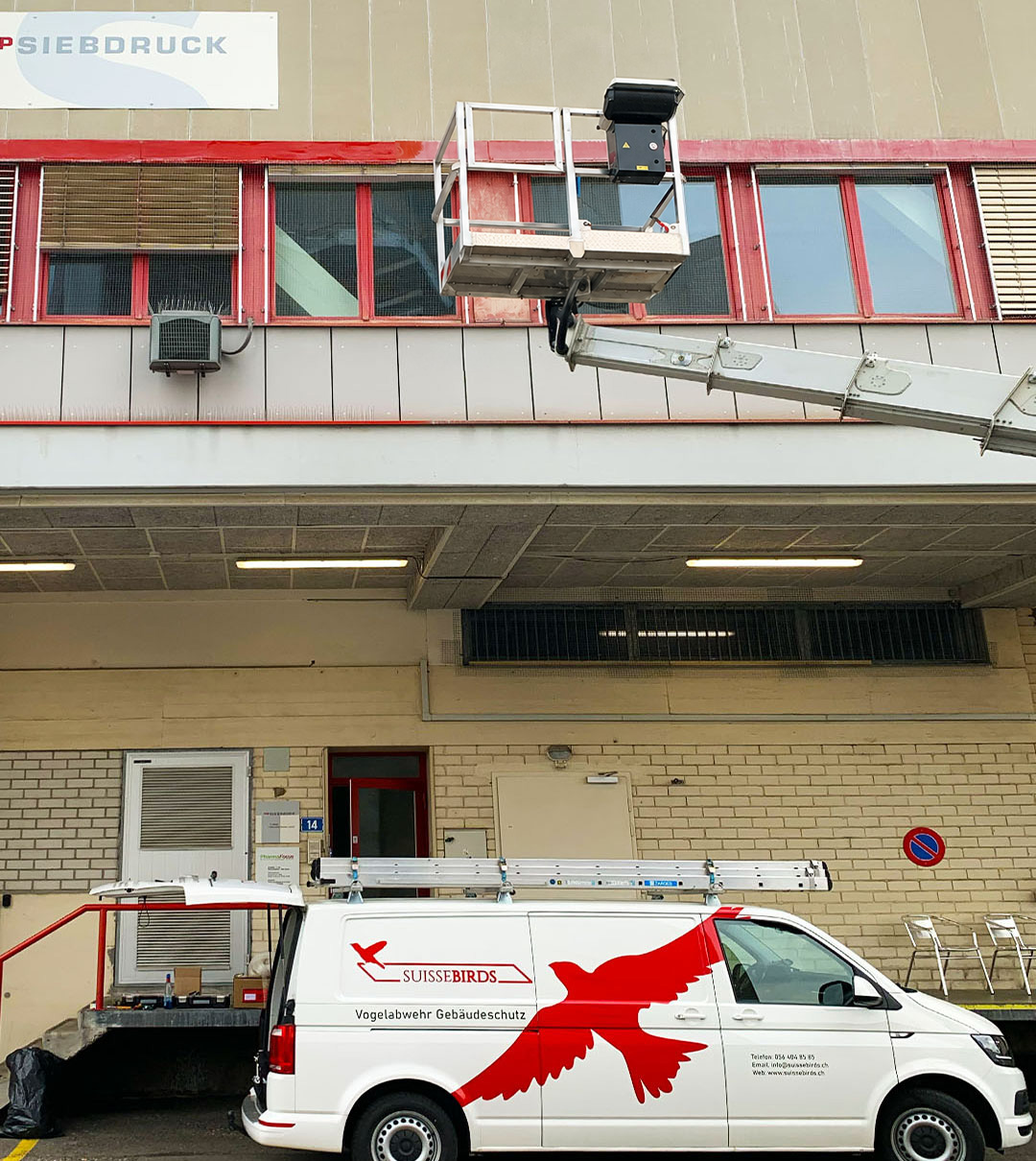 Hubarbeitsbühne und Suisse Birds Servicefahrzeug bei Arbeiten an einer Gewerbefassade