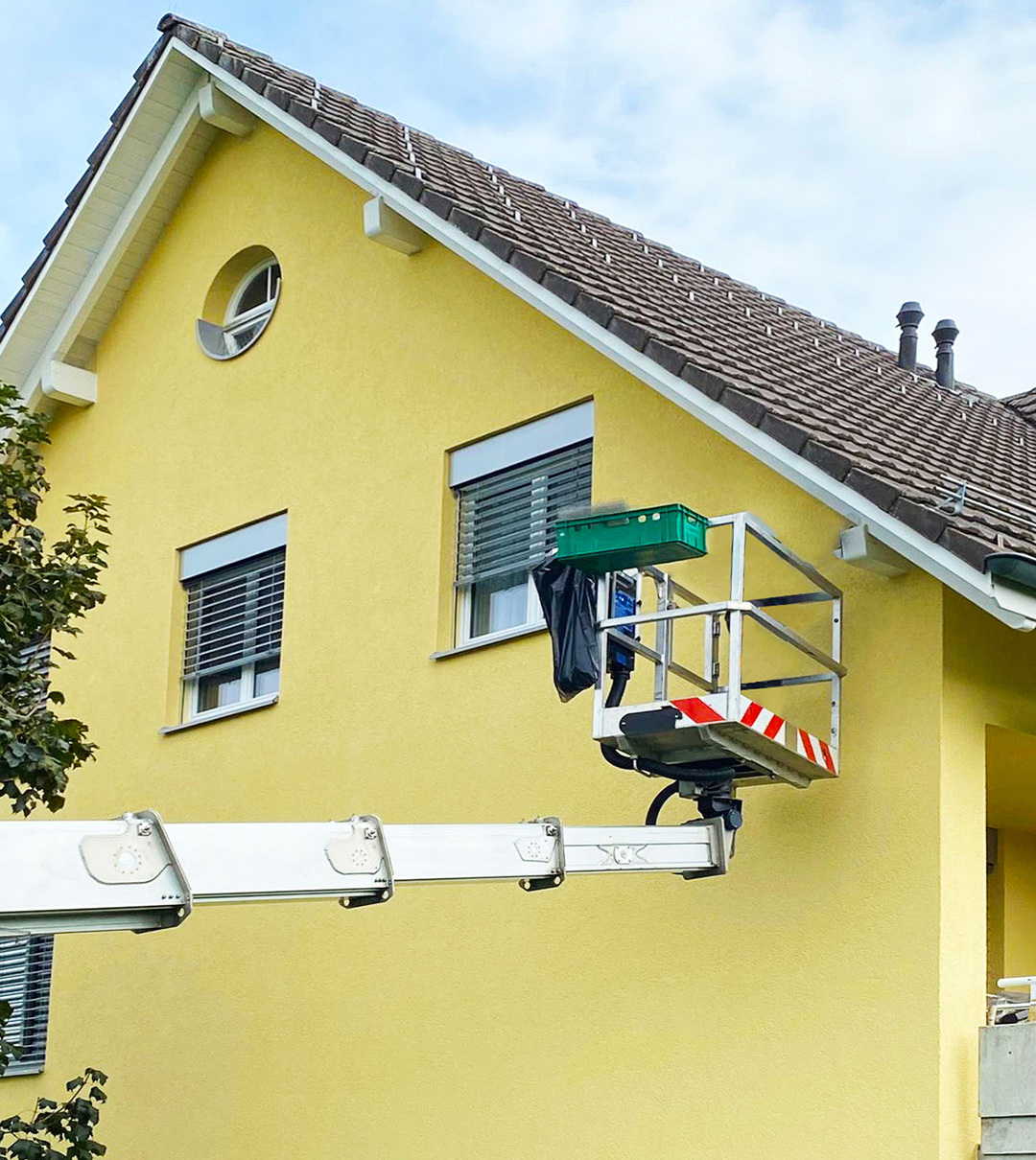 Mitarbeiter auf einer Hubarbeitsbühne an Fassade und Dachkante eines Wohnhauses