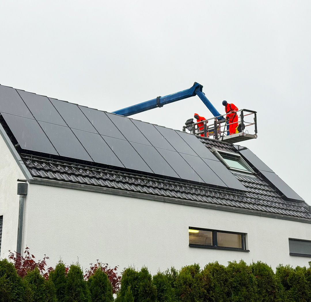 Mitarbeiter auf einer Hebebühne bei Arbeiten neben einer Photovoltaikanlage