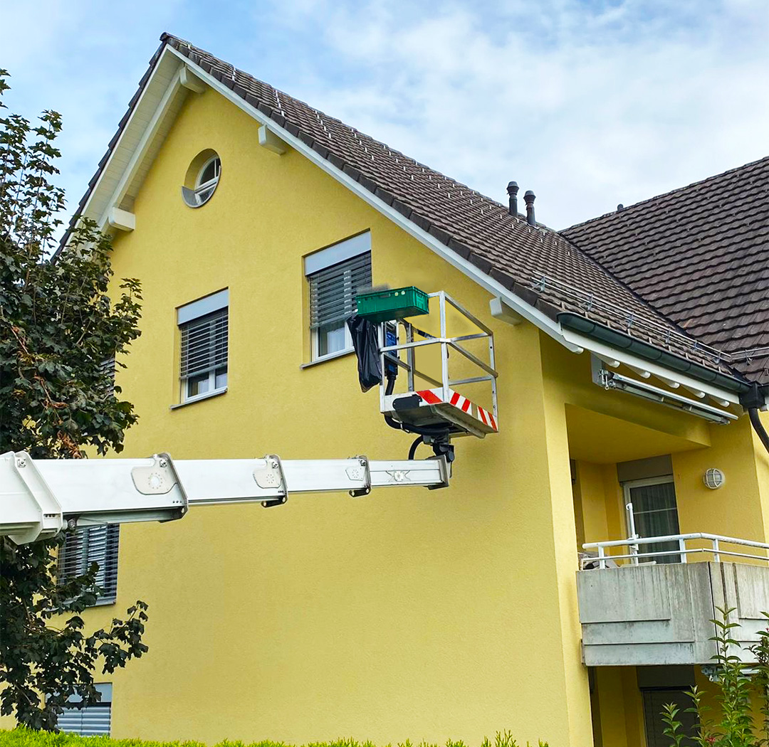 Mitarbeiter auf einer Hebebühne bei Arbeiten an einer Wohnhausfassade