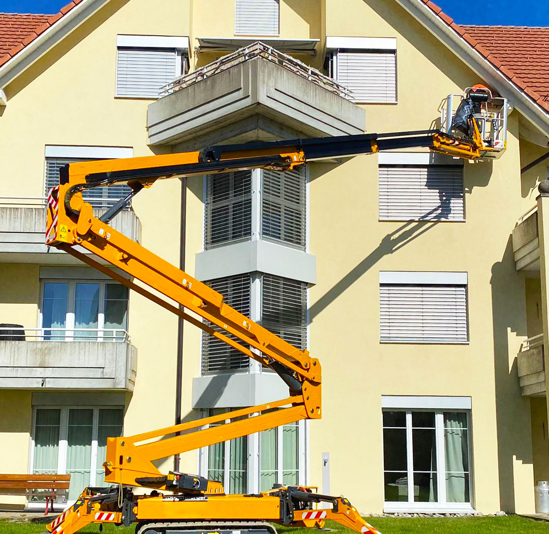 Raupenhebebühne bei Arbeiten an Balkon und Fassade eines Wohngebäudes