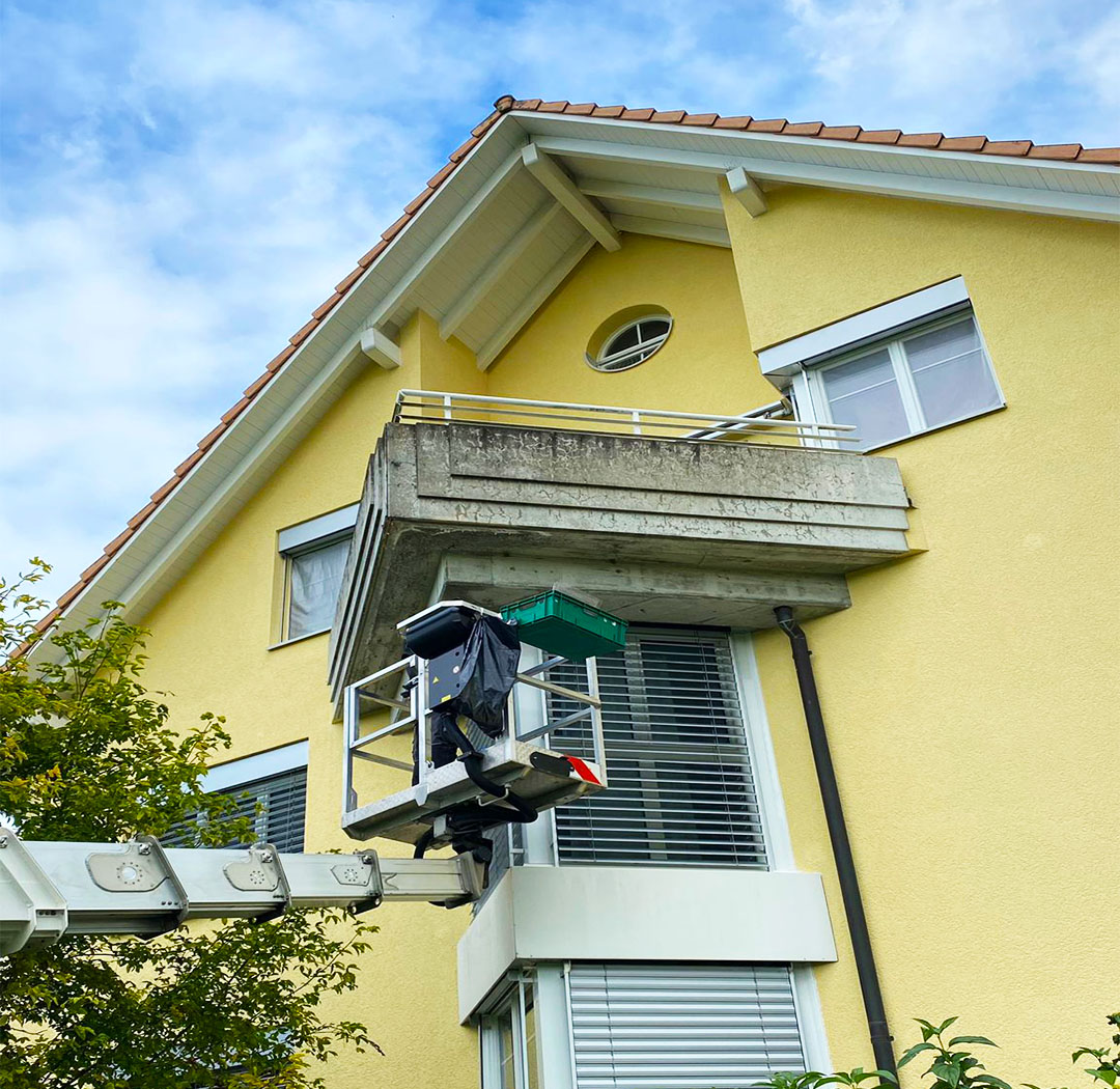 Mitarbeiter auf einer Hebebühne bei Arbeiten an Balkon und Fassade