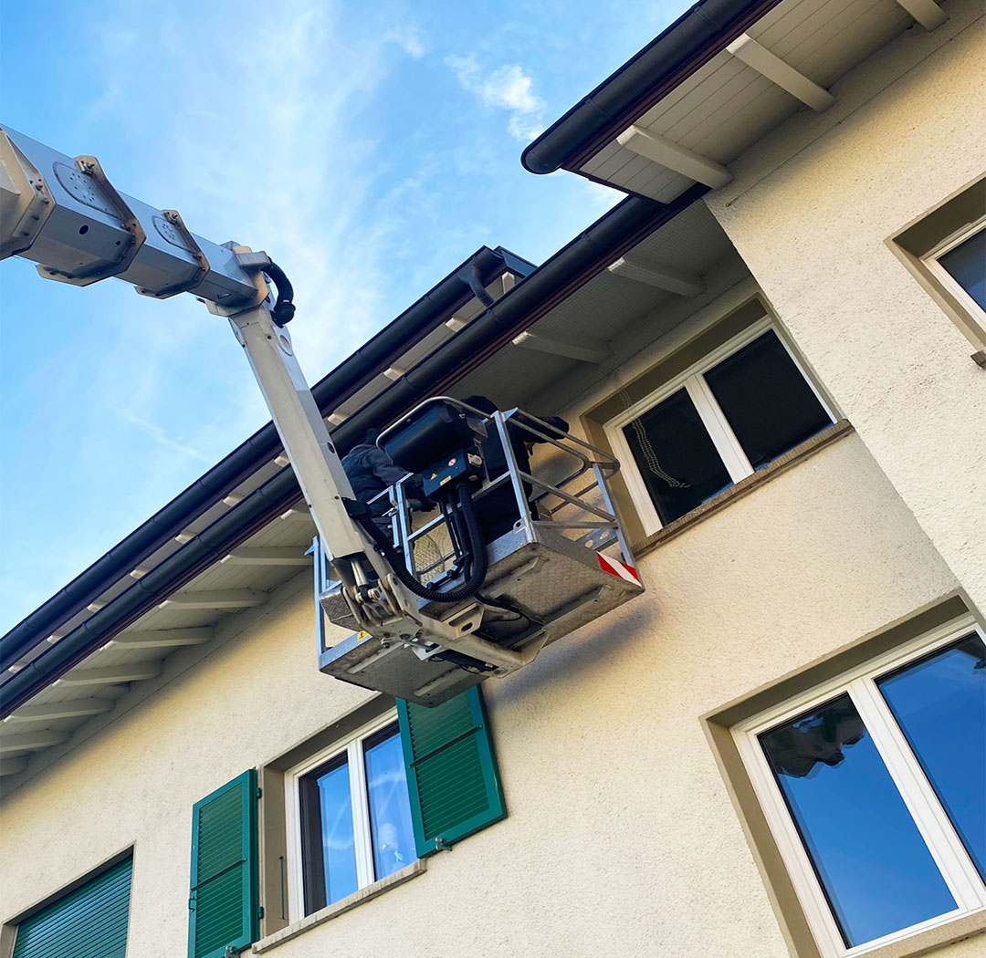 Mitarbeiter auf einer Hebebühne bei Arbeiten an Dachrand und Fassade eines Wohnhauses
