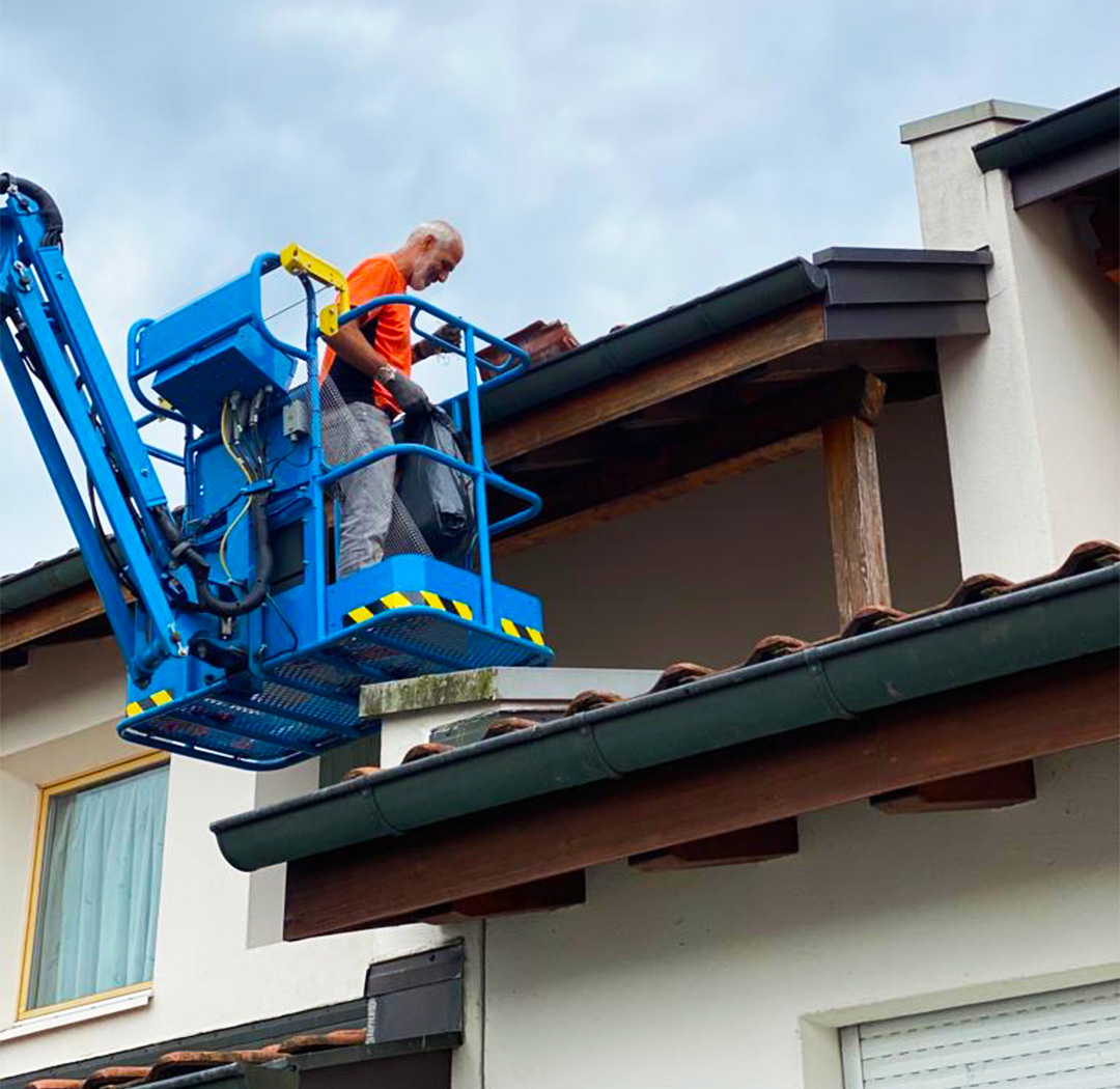 Mitarbeiter auf einer blauen Hebebühne bei Arbeiten an einer Dachkante