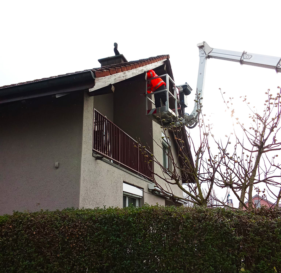 Mitarbeiter im Arbeitskorb bei Arbeiten an Dach und Fassade eines Wohnhauses