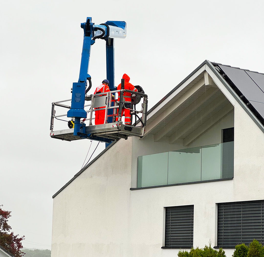 Mitarbeiter im Arbeitskorb bei Arbeiten an der Dachkante eines modernen Wohnhauses
